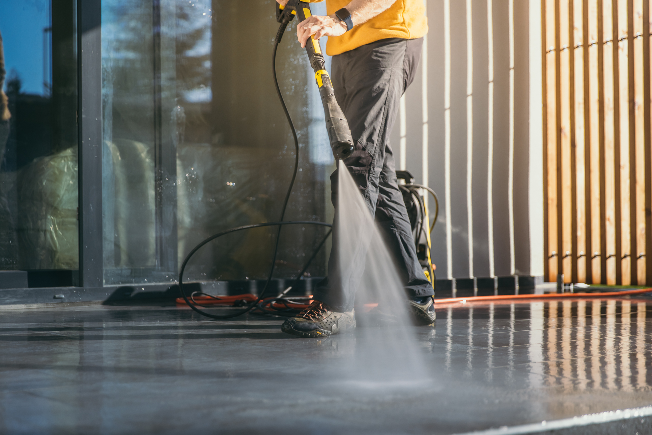 Man cleaning the terrace tiles of the apartment with squirt gun